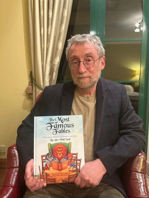 Alex Wolf Neuk holding a book titled 'The Most Famous Fables' in a room with curtains and a lamp.